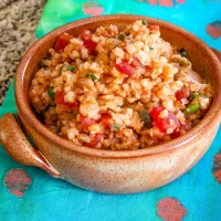 Cooked rice dish with chopped vegetables and tomato chunks in a brown bowl.