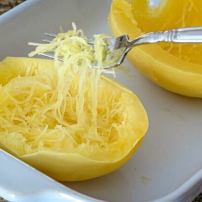 Spaghetti squash in a baking dish cooked in the microwave—strands lifted with a fork.