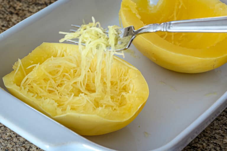 Spaghetti squash in a baking dish cooked in the microwave—strands lifted with a fork.