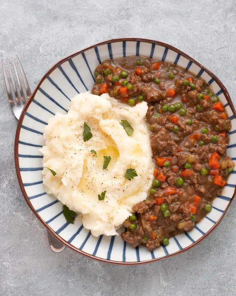 Tender beef stew with carrots and peas served with creamy mashed potatoes.