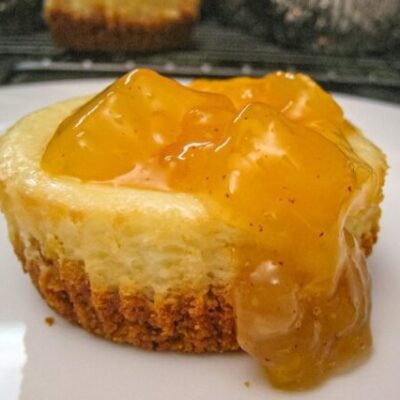 A delicious mini cheesecake on a plate with peach topping.