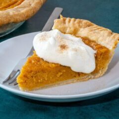 A slice of sweet potato pie on a plate with a dollop of whipped cream and cinnamon sugar.