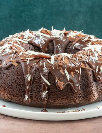 Moist chocolate bundt cake on a plate, decorated with a chocolate glaze and chocolate shards.