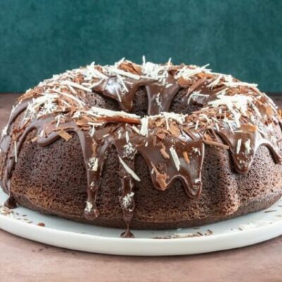 Moist chocolate bundt cake on a plate, decorated with a chocolate glaze and chocolate shards.