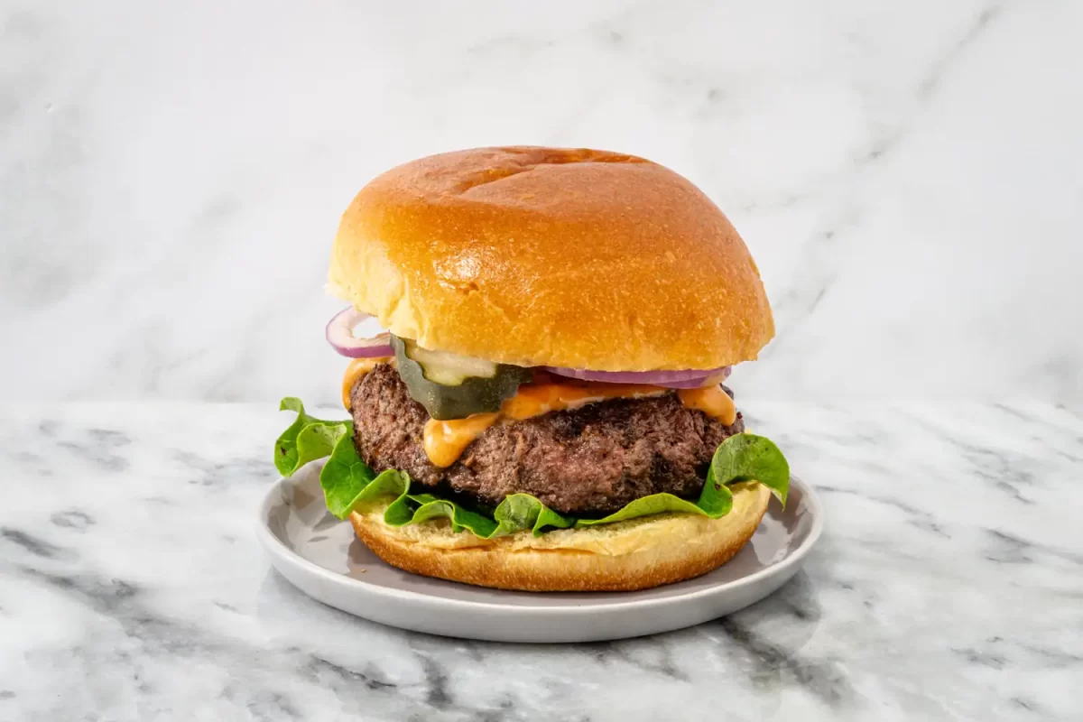 A mozzarella burger with lettuce, pickles, and tomatoes, on a brioche bun.