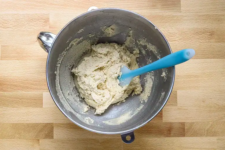 Creamy mashed potato mixture in a metal bowl with a blue spatula.