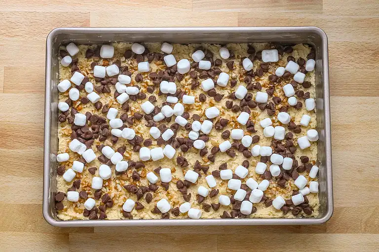 Sweet dessert mixture with chocolate chips and mini marshmallows in a baking pan.