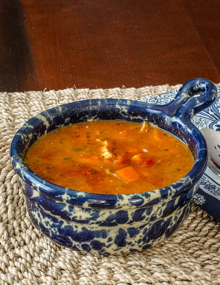 Warm bowl of vegetable soup in a decorative blue and white ceramic dish.