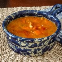 Pottery bowl filled with vegetable soup with visible carrots and herbs.