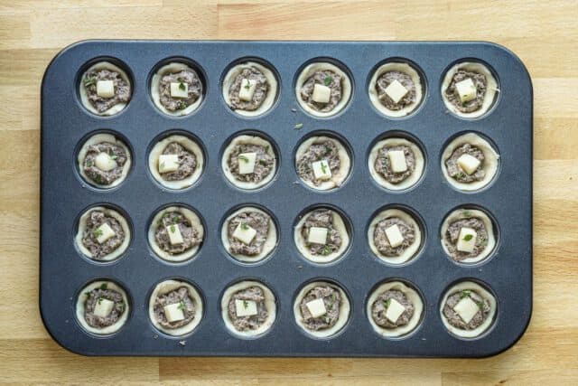 Mushroom tarts with a cube of fontina cheese and thyme, ready to bake.