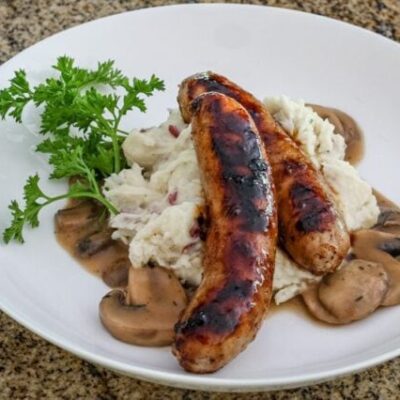 Mushroom sauce with beef stock, garlic, and a splash of beer shown with mashed potatoes and grilled sausages.
