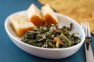 a dish of mustard greens with bacon and sliced cornbread