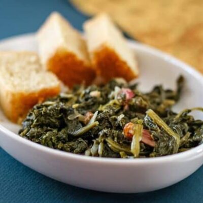a dish of mustard greens with bacon and sliced cornbread