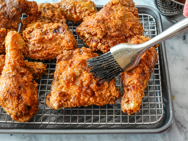 Fried chicken with hot sauce being brushed onto it.