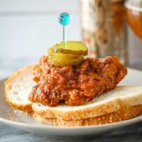 Plate of Nashville hot chicken on bread with pickles.