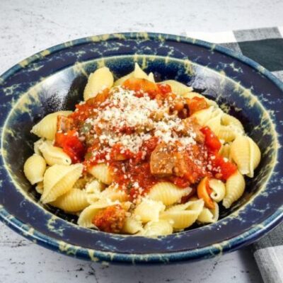 A wide bowl with Neapolitan sauce with sausage and tomatoes over pasta shells.