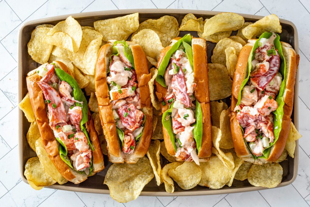 Four generously stuffed lobster rolls surrounded by potato chips.