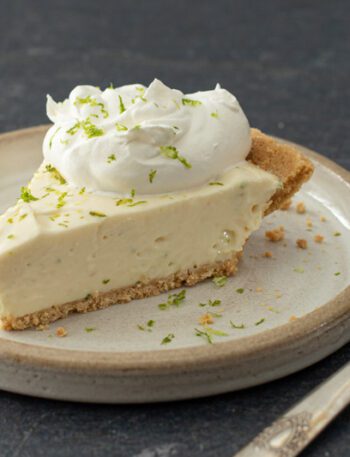 A slice of no-bake key lime cheesecake with whipped cream and lime zest.