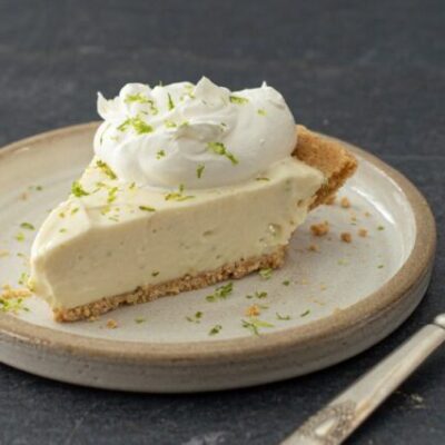 A slice of no-bake key lime cheesecake with whipped cream and lime zest.