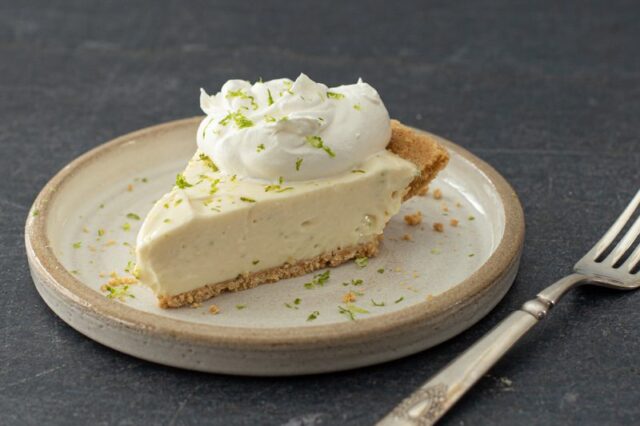 A slice of no-bake key lime cheesecake with whipped cream and lime zest.