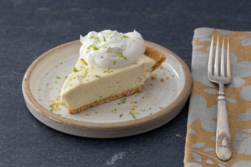 A no-bake key lime cheesecake with a dollop of whipped cream and lime zest.