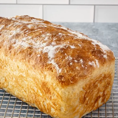 Bread loaf on cooling rack with a crusty top and dusted with flour.