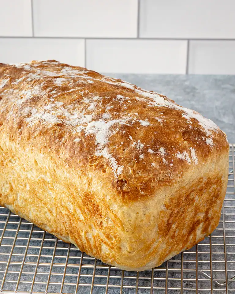 Bread loaf on cooling rack with a crusty top and dusted with flour.
