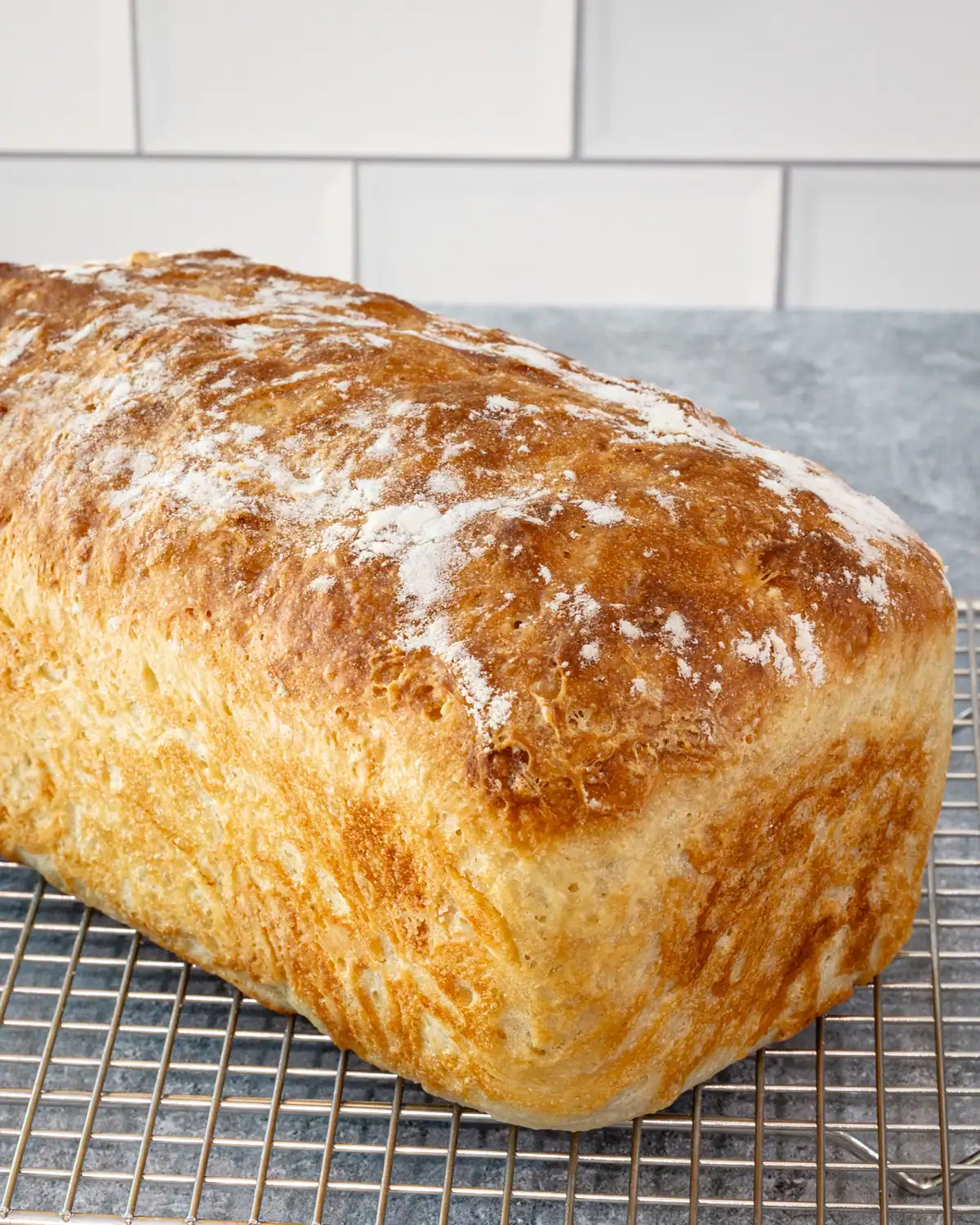 Bread loaf on cooling rack with a crusty top and dusted with flour.