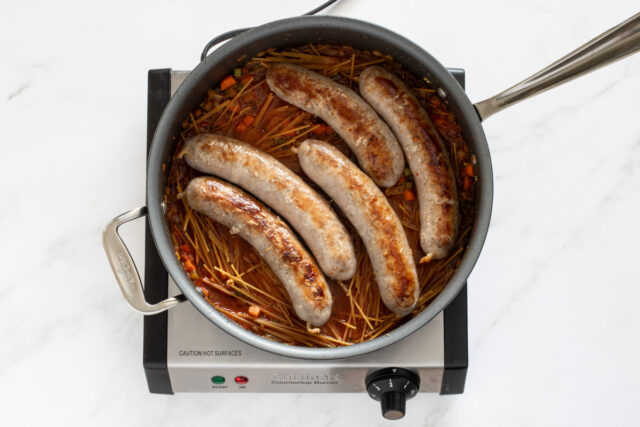 Adding water, dry spaghetti, and sausages to the pan to make the one pot spaghetti and sausage meal.