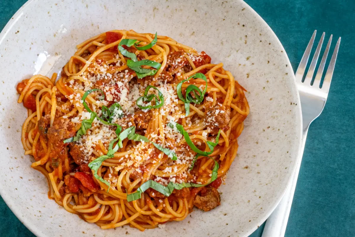 Spaghetti with meat sauce, topped with grated cheese and fresh basil.