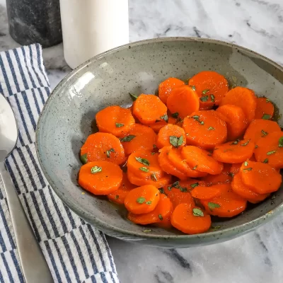 Sweet glazed carrots garnished with chopped herbs in a rustic bowl.