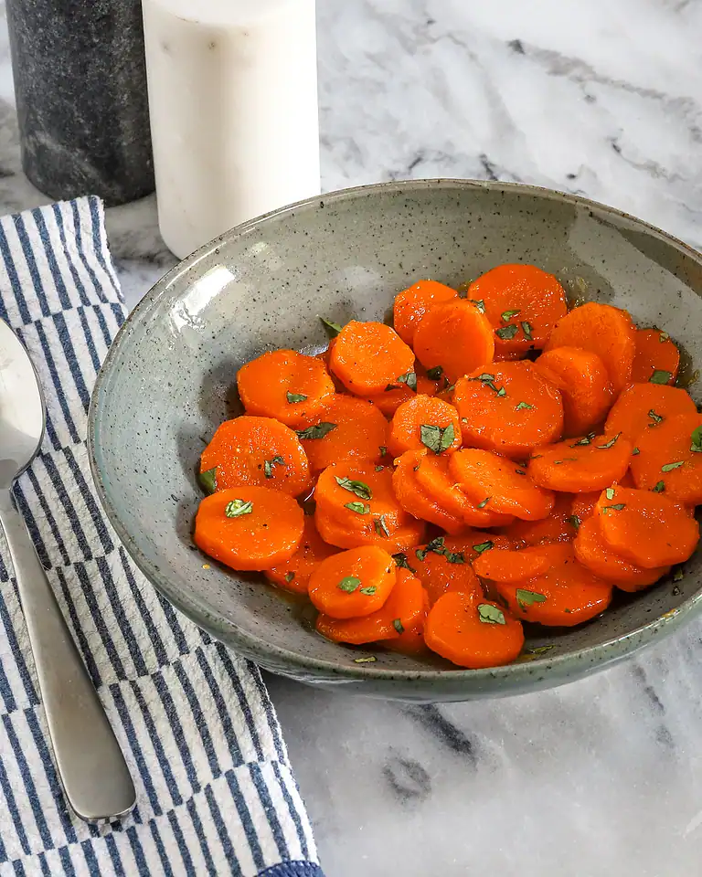 Sweet glazed carrots garnished with chopped herbs in a rustic bowl.