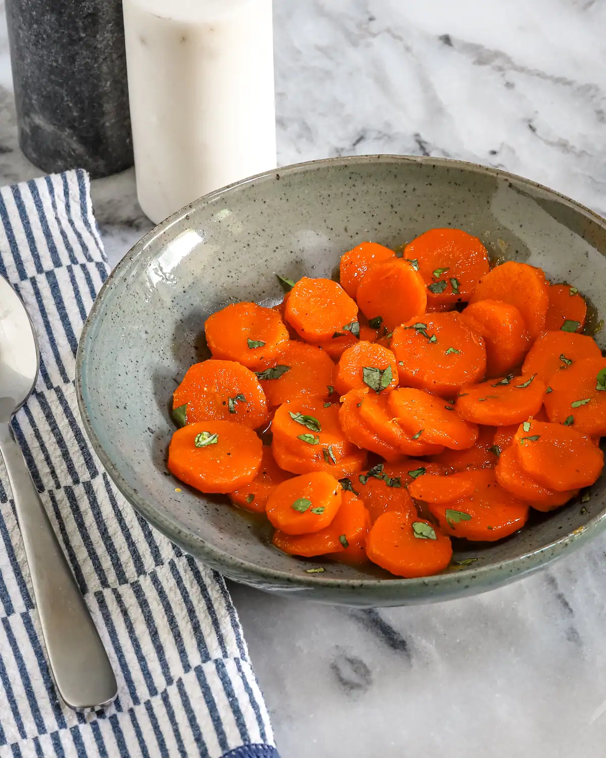 Sweet glazed carrots garnished with chopped herbs in a rustic bowl.