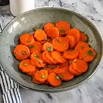 Roasted carrots with chopped herbs in a ceramic bowl.
