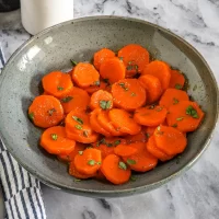 Roasted carrots with chopped herbs in a ceramic bowl.