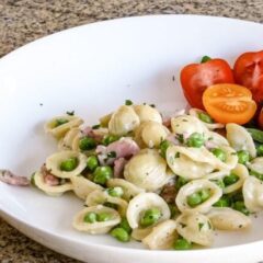 A pasta bowl with a dish of orecchiette with ham, peas, and Parmesan cheese.
