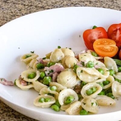 A pasta bowl with a dish of orecchiette with ham, peas, and Parmesan cheese.