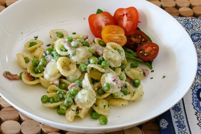 A closeup photo of orecchiette with peas, ham, cream, and Parmesan cheese.