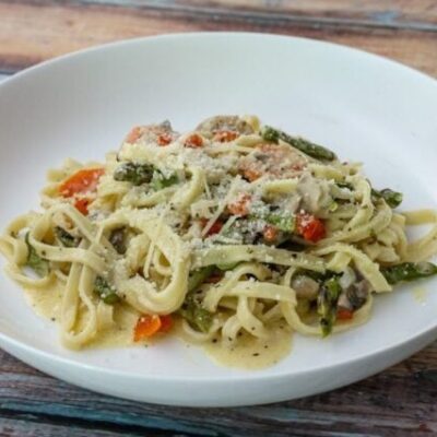 a bowl of pasta with asparagus and ham in a parmesan cheese sauce