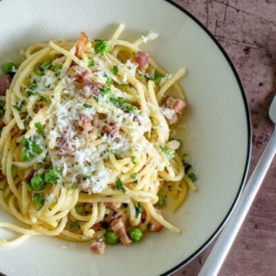 pasta with pancetta and peas on a plate with pecorino romano cheese garnish