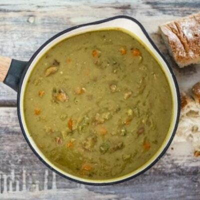 A saucepan with pea soup and crusty bread on the side