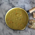 A pan of pea soup with bread on the side.