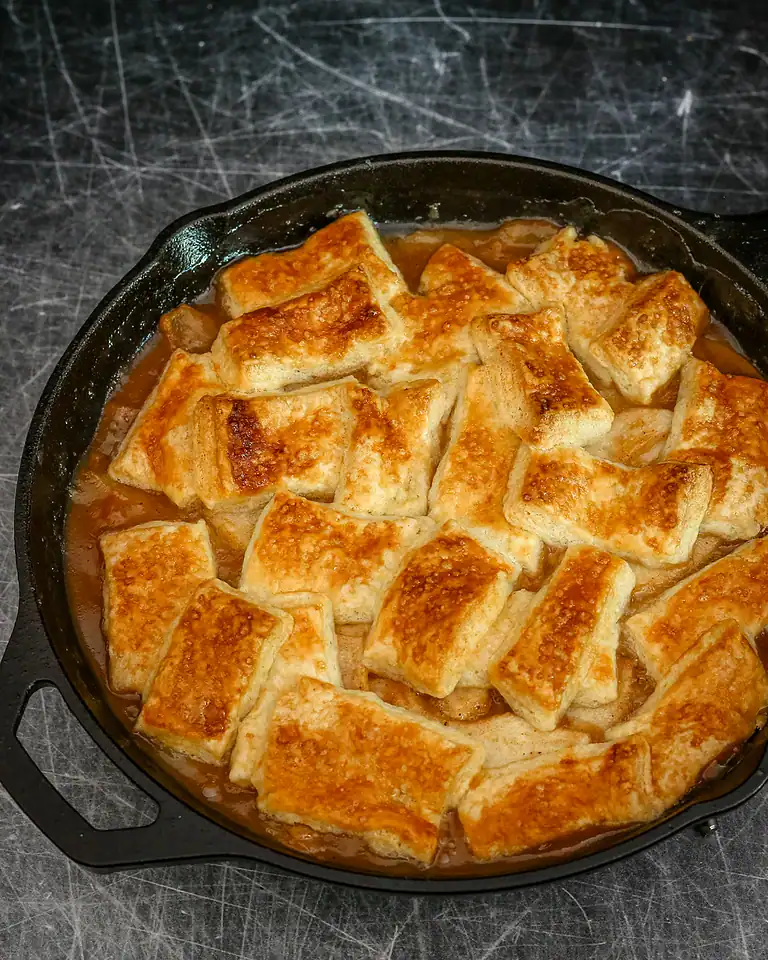 Crispy fried bread pieces soaking in sauce in a cast iron skillet.