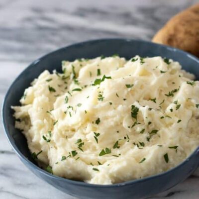 A serving bowl of mashed potatoes with parsley garnish