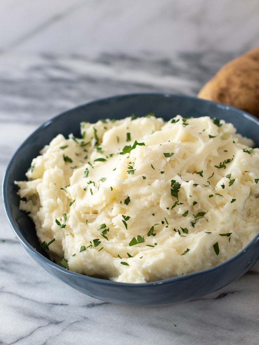A serving bowl of mashed potatoes with parsley garnish