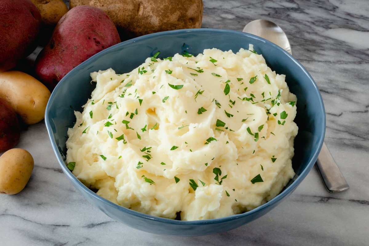 Mashed potatoes in a serving bowl wit a spoon and a garnish of parsley.