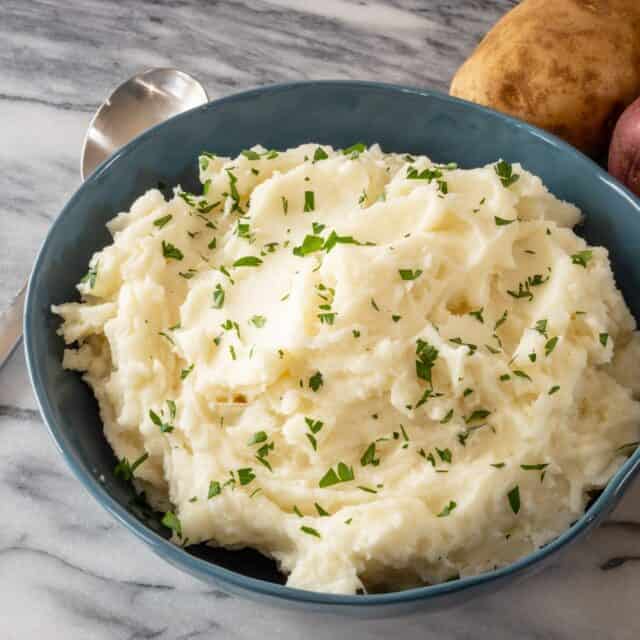 Classic mashed potatoes in a serving bowl with parsley garnish.
