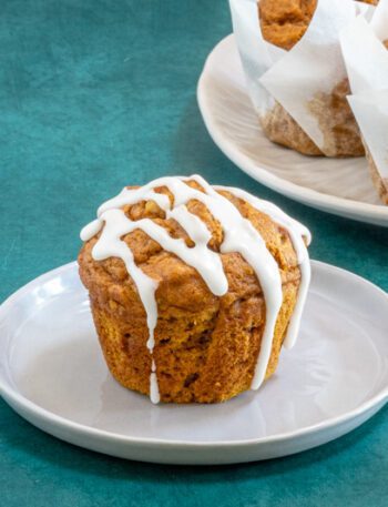 A pumpkin muffin with icing and more pumpkin muffins in the background