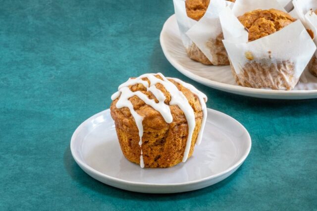 A pumpkin muffin with icing and more pumpkin muffins in the background