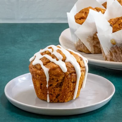 Golden brown muffin topped with white icing on a small white plate.